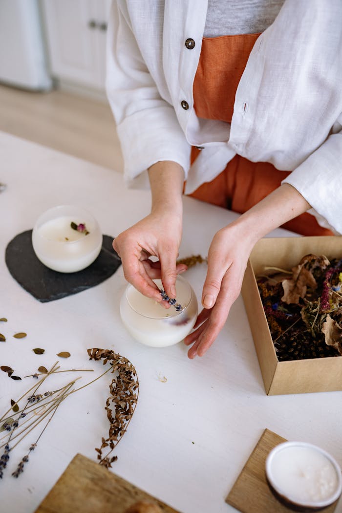 Hands crafting candles with dried flowers in an artisanal workshop setting.